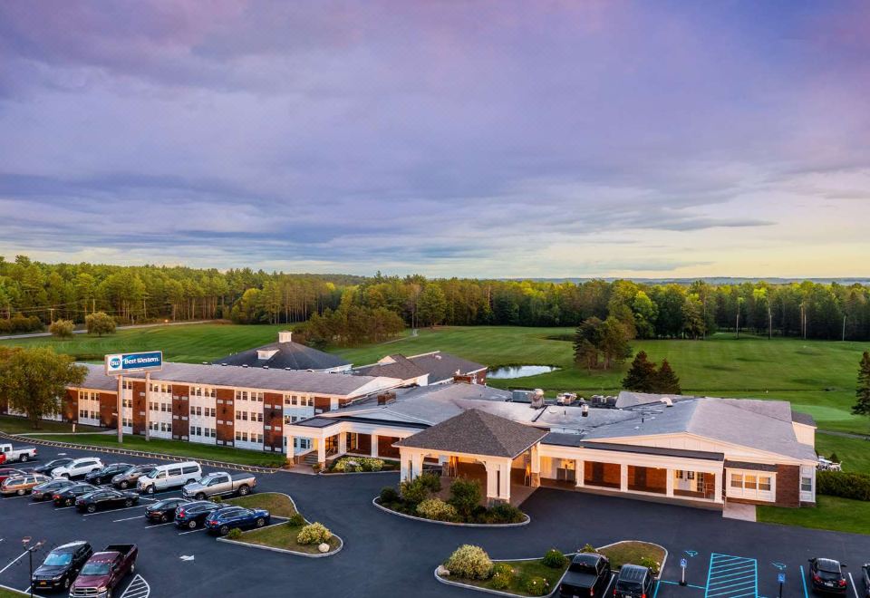 an aerial view of a large hotel surrounded by trees and grass , with a parking lot in front of it at Best Western University Inn