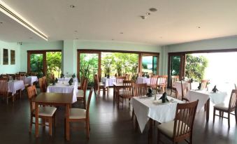 a large dining room with wooden tables and chairs , all set for a meal , surrounded by windows that offer a view of the outdoors at Siam Triangle Hotel