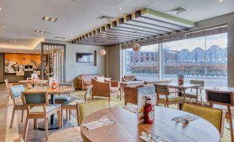 a restaurant with wooden tables and chairs , a large window , and a bottle on the table at Premier Inn Hereford City Centre (Old Market)