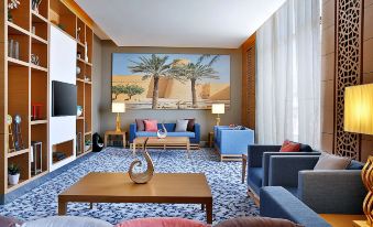 a modern living room with a blue couch , coffee table , and a large painting on the wall at Hilton Garden Inn Tabuk