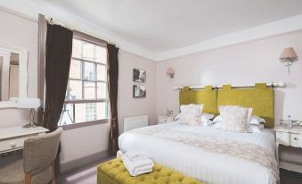a large bed with a yellow headboard and white linens is situated in a room with a window at The Globe