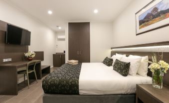 a modern hotel room with a bed , desk , and tv , decorated in white and gray colors at Morphettville Motor Inn