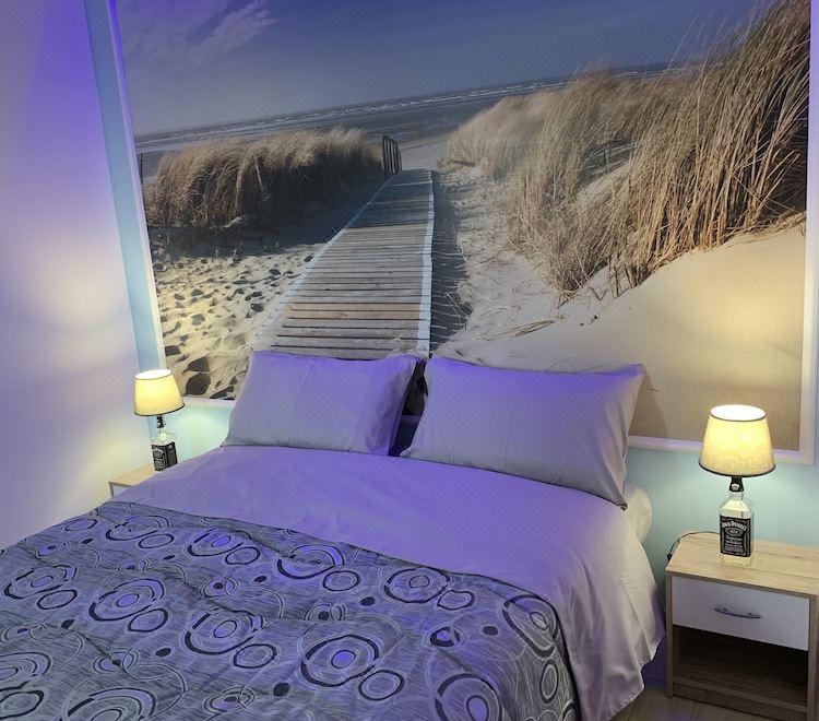 a bed with a blue and white comforter is placed in front of a wall mural depicting a sandy beach at The Lux