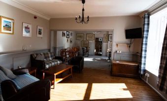 a spacious living room with hardwood floors , a couch , chairs , and a dining table . also a television in the room at The Kirkmichael Hotel