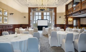 a large dining room with multiple round tables covered in white tablecloths , and a projector screen set up in the center of the room at Delta Hotels Breadsall Priory Country Club