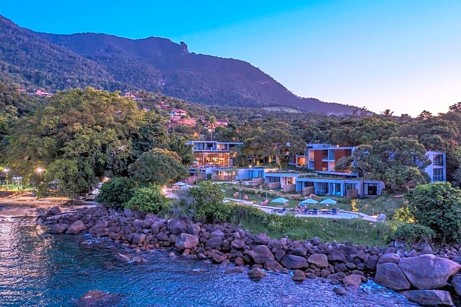 a modern resort with multiple buildings and a beach in the foreground , surrounded by lush greenery and mountains in the background at Wyndham Ilhabela Casa di Sirena