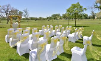 a wedding ceremony is taking place on a grassy field , with white chairs adorned with yellow ribbons at DoubleTree by Hilton Hotel Grand Junction