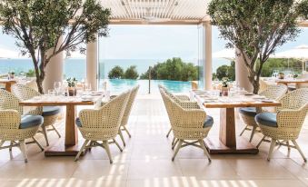 a large dining room with multiple tables and chairs , as well as a pool in the background at Ikos Oceania