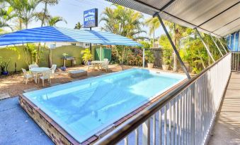 a small , rectangular pool with a blue and white umbrella is surrounded by a patio area at Blue Shades Motel