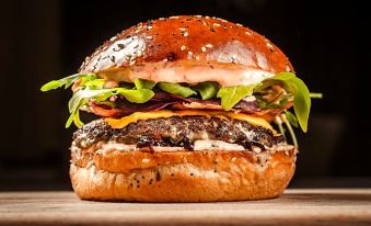 a close - up of a delicious cheeseburger on a bun with various toppings , placed on a wooden cutting board at Royal Airport Hotel