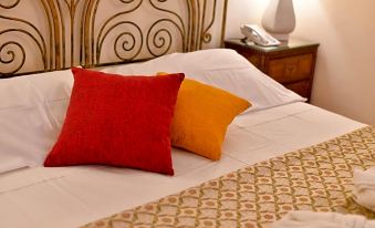 a bed with two red pillows and a white comforter , set against a wall with a headboard at Grand Hotel Terme di Augusto