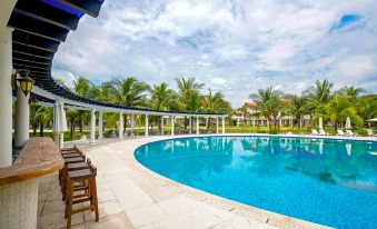 a large outdoor swimming pool surrounded by palm trees , with lounge chairs and umbrellas placed around the pool at Seava Ho Tram Beach Resort