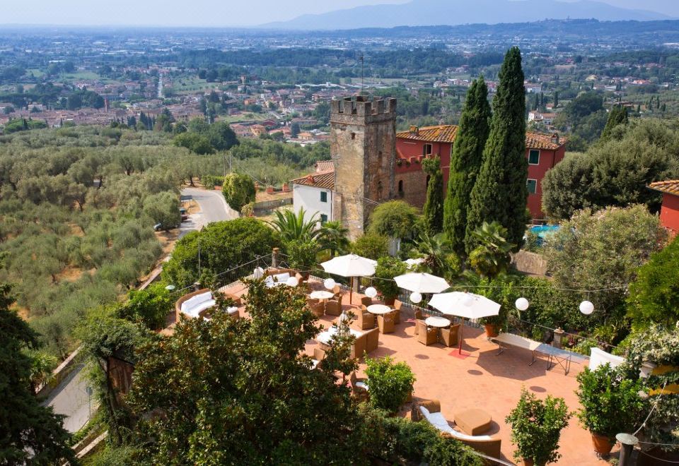 an aerial view of a garden with a tall tower and various plants , umbrellas , and tables set up for outdoor dining at Hotel Villa Sermolli