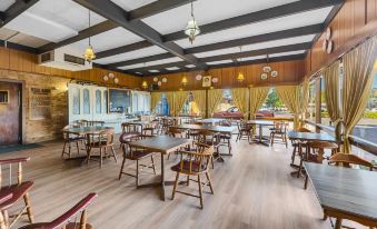 a large dining room with wooden tables and chairs , surrounded by windows and a chandelier at Plainsman Motel