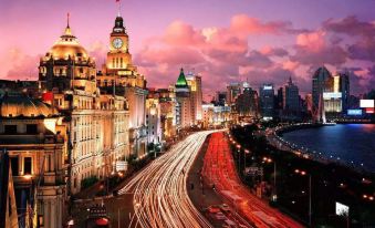 At night, a city skyline with illuminated buildings, including a clock tower at Meego Yes Hotel