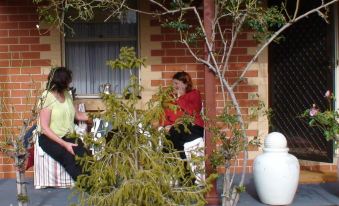 two women are sitting on a porch , one is talking on her phone while the other sits nearby at Albury Cottages