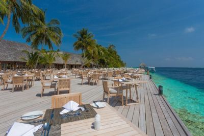 a wooden deck with tables and chairs , palm trees , and the ocean in the background at Vilamendhoo Island Resort & Spa