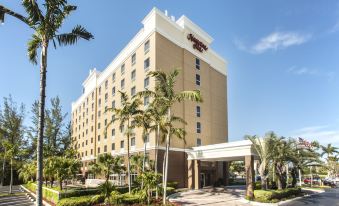 a large hotel with a white exterior and palm trees in front of it , under a clear blue sky at Hampton Inn Hallandale Beach-Aventura