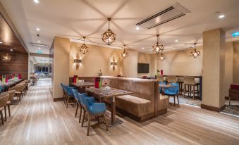 a modern bar area with wooden flooring , blue chairs , and tables , along with pendant lights and hanging lights at Hampton by Hilton Kahramanmaras