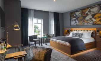 a modern bedroom with a large bed , chairs , and a painting on the wall , along with a dining area and table at Oriel House Hotel