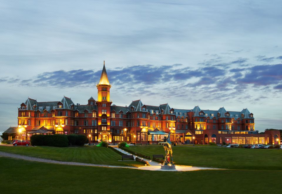 a large , modern building with multiple floors and balconies , surrounded by green grass and trees , during the evening at Slieve Donard