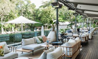 a modern outdoor lounge area with white furniture , including couches , chairs , and umbrellas , surrounded by lush greenery at Crystalbrook Byron