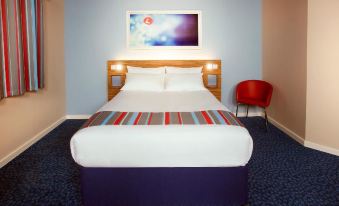 a bed with a blue headboard and white sheets is in a room with a red chair at Travelodge Sleaford