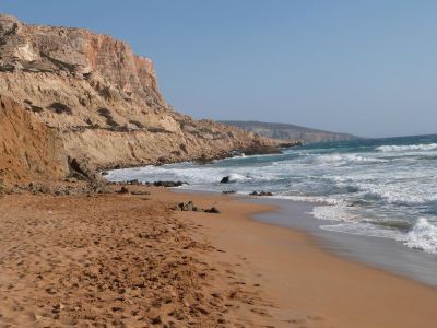 a sandy beach near a cliff , with waves crashing against the shore and a group of people enjoying the sunny day at Valley Village