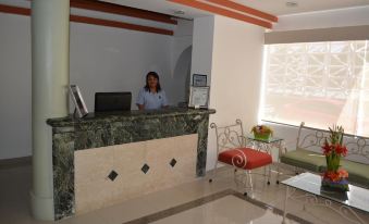 a receptionist standing behind a marble counter in a modern office with white walls and orange curtains at Hotel del Parque