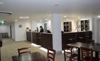 a man standing behind a counter in a restaurant , preparing food and drinks , while others sit at the tables at Best Western Plus London Croydon Aparthotel