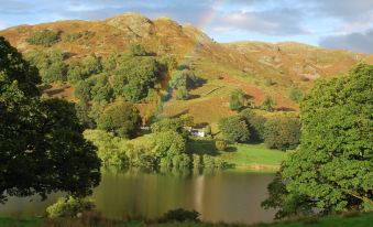 a picturesque landscape with a lake surrounded by hills and a rainbow in the sky at The Punchbowl Hotel