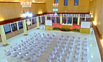 an empty , spacious event hall with wooden walls and large chandeliers , filled with white chairs arranged in rows for an outdoor event at Danau Dariza Resort Hotel - Cipanas Garut