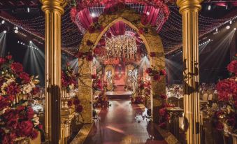 A ballroom is decorated with red and gold lighting, and flowers are placed on the floor for an event at Gems Cube International Hotel