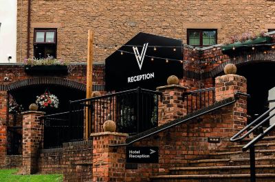 a brick building with a reception sign and stairs leading up to it , surrounded by trees at Village Hotel Liverpool