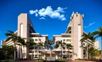 a large white building with a tall tower is surrounded by palm trees and a red parking lot at Hyatt Vacation Club at Hacienda del Mar