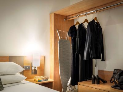 a hotel room with a bed , a closet , and a tv . also a coat rack in the room at Ibis Melbourne Hotel and Apartments