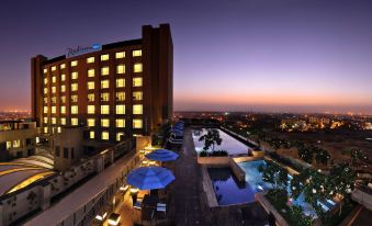 a hotel with a large outdoor pool and patio area , illuminated by the setting sun at Radisson Hotel New Delhi Paschim Vihar