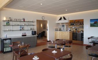 a modern restaurant with wooden tables and chairs , a bar area , and various bottles on the shelves at Hotel Flokalundur