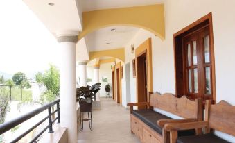 a long , covered walkway with wooden benches and a balcony , leading to a building with yellow and white walls at Donaji