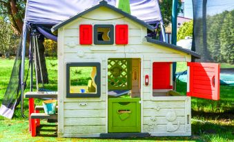 a colorful playhouse with a red door and windows is set up on a grassy lawn at Kosmik