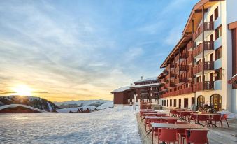 a snow - covered mountain with a building and a restaurant on top of it , surrounded by a blue sky at Hotel l'Eden des Cimes - Vacances Bleues - Belle Plagne 2100