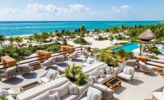 a large terrace with multiple couches and chairs , surrounded by lush greenery and overlooking a beautiful blue ocean at Chable Maroma