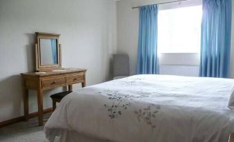 a clean and well - organized bedroom with a white bed , blue curtains , and a wooden dresser at Tayberry