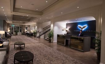 a modern hotel lobby with a check - in desk , reception area , and a large screen displaying a man 's image on the wall at Seamill Hydro Hotel