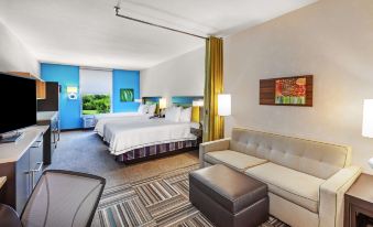 a modern hotel room with a large bed , couch , and desk , all set against blue walls at Home2 Suites by Hilton Gonzales