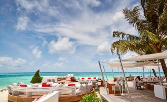 a tropical beach with umbrellas , lounge chairs , and palm trees under a blue sky dotted with clouds at LUX* South Ari Atoll