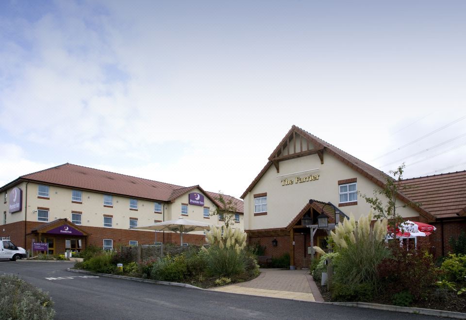a two - story hotel building with a red - brick facade and large windows , surrounded by greenery and a clear blue sky at Premier Inn Grantham