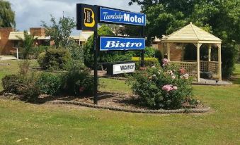 a sign for a motel and a bistro in front of a wooden gazebo surrounded by grass at Toora Lodge Motel