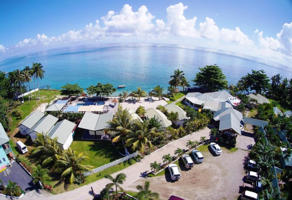 a panoramic view of a resort area with buildings , cars , and palm trees near the ocean at Le Uaina Beach Resort