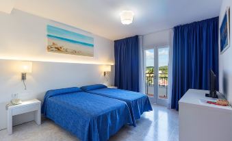 a bedroom with a blue bed , white curtains , and a painting of the ocean on the wall at Hotel Cala Murada